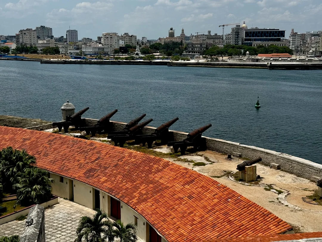 Historic coastal cannons overlooking Havana Bay from Castillo de los Tres Reyes del Morro in Cuba, with a panoramic view of the city skyline across the water. A blend of colonial history and urban charm.