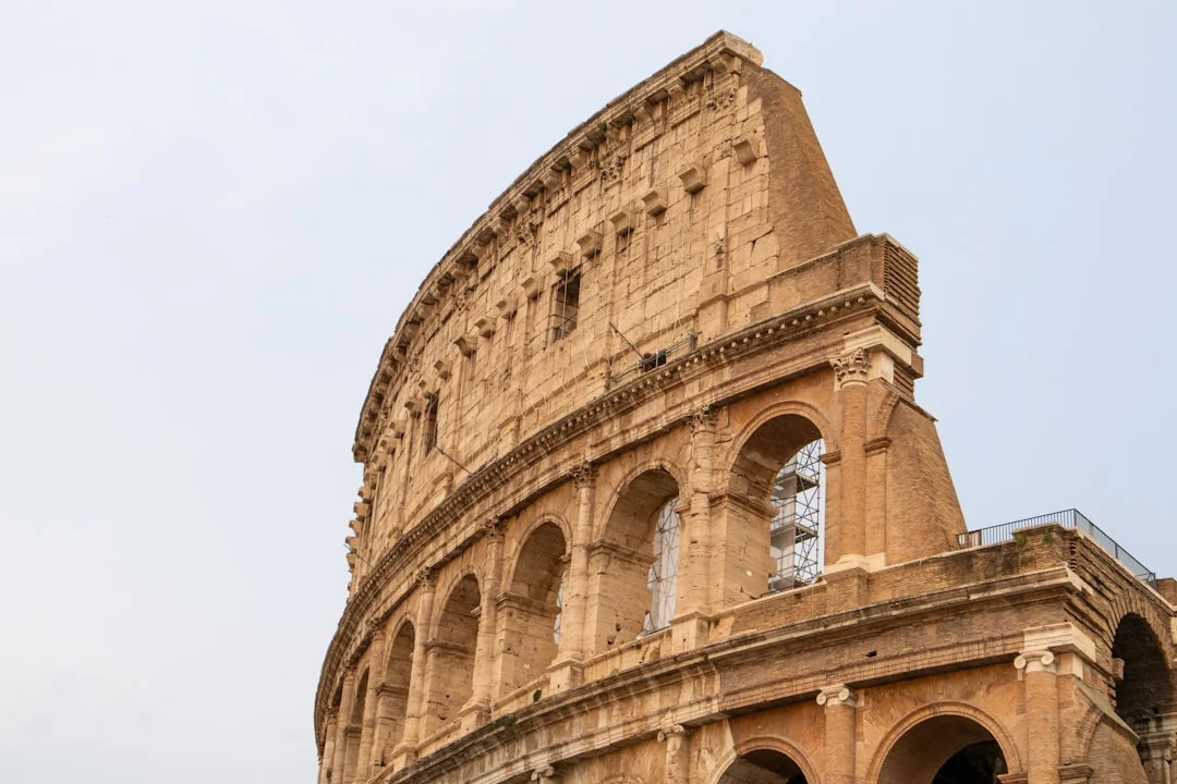 A close view of the Colosseum’s weathered outer wall reveals tiered arches and ancient stonework silhouetted against a pale Roman sky.