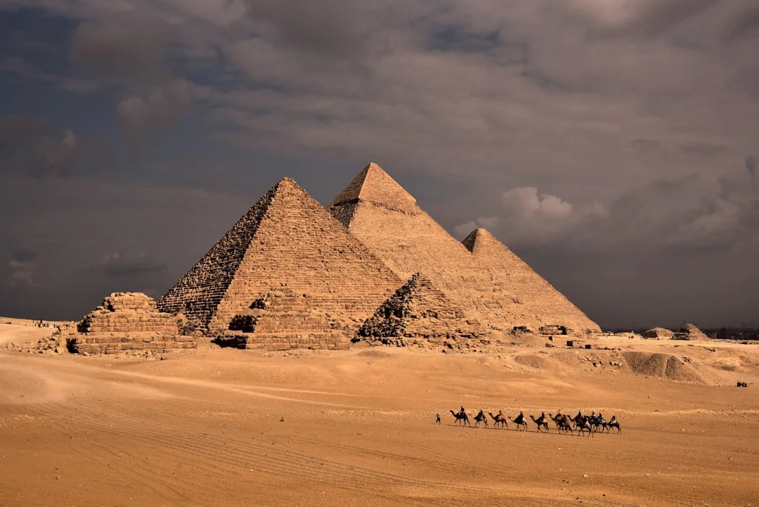 a group of people riding camels in front of three pyramids